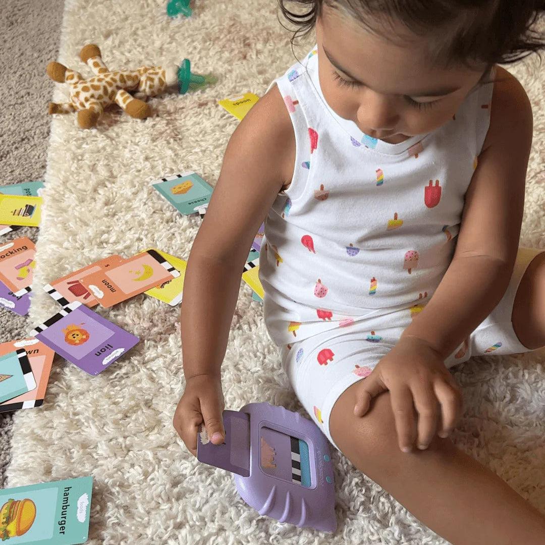 Malé dítě si samostatně hraje s mluvící čtečkou a kartami Kinderspeech, které jsou rozprostřené na koberci pro hravé učení slovíček.