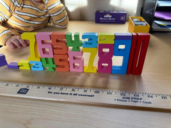 Sestava barevných dřevěných číslic Kinderspeech vyrovnaných vedle pravítka pro hravé učení matematiky a logiky.
